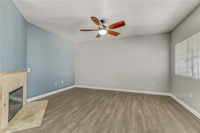 unfurnished living room featuring ceiling fan, wood-type flooring, and a tiled fireplace