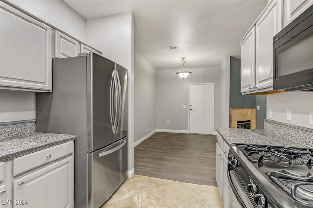 kitchen with pendant lighting, white cabinets, light tile patterned floors, appliances with stainless steel finishes, and a tiled fireplace