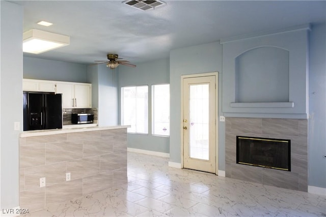 kitchen featuring backsplash, black fridge, ceiling fan, a tile fireplace, and white cabinetry