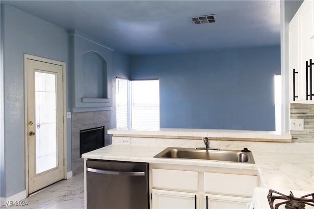 kitchen with stove, stainless steel dishwasher, sink, a tile fireplace, and white cabinetry