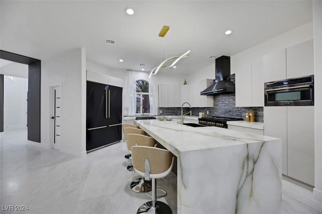 kitchen featuring stainless steel oven, a spacious island, wall chimney exhaust hood, and high end black refrigerator