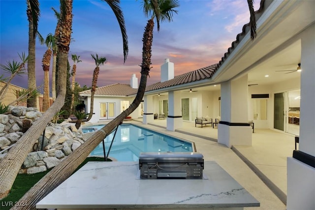 pool at dusk featuring ceiling fan, a patio area, french doors, and a hot tub