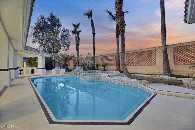 pool at dusk featuring an in ground hot tub and a patio