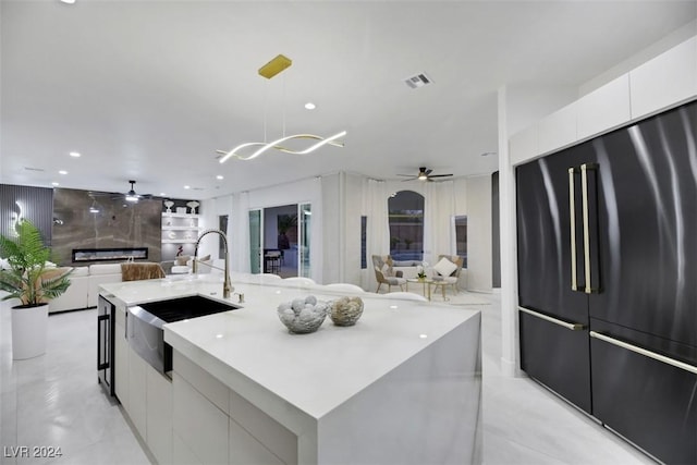 kitchen featuring sink, a large island with sink, decorative light fixtures, white cabinets, and built in fridge