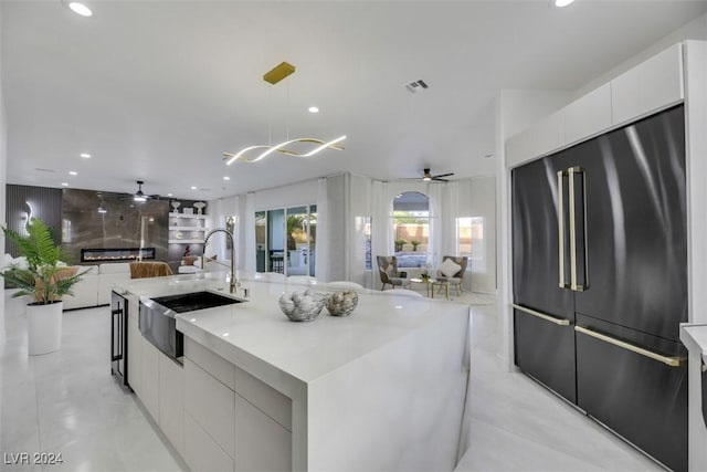 kitchen with stainless steel built in refrigerator, a center island with sink, sink, decorative light fixtures, and white cabinetry