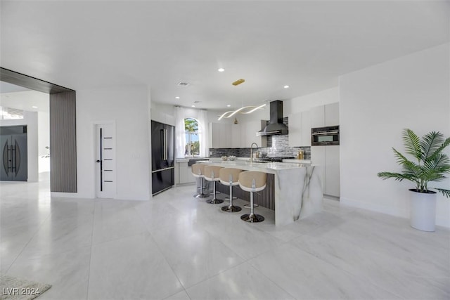 kitchen featuring wall chimney range hood, an island with sink, fridge, high quality fridge, and white cabinets