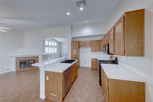 kitchen featuring stainless steel appliances, ceiling fan, sink, a center island with sink, and a tiled fireplace