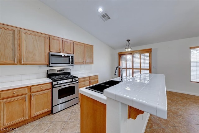 kitchen with appliances with stainless steel finishes, sink, pendant lighting, tile countertops, and an island with sink