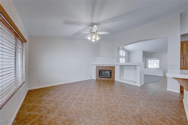 unfurnished living room featuring a tile fireplace, light tile patterned floors, and ceiling fan