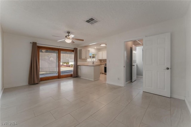 unfurnished living room featuring ceiling fan, sink, light tile patterned flooring, and a textured ceiling