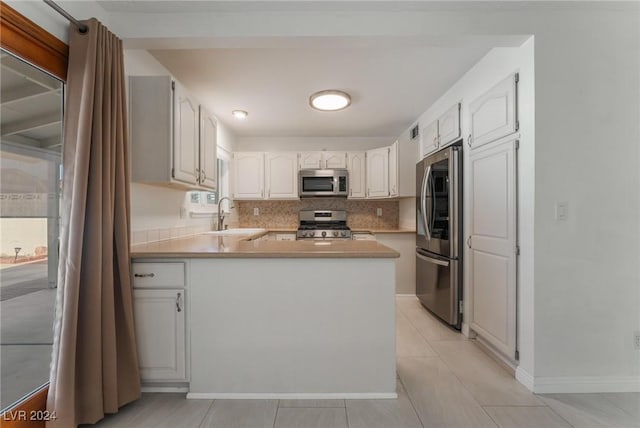 kitchen featuring sink, light tile patterned flooring, kitchen peninsula, white cabinets, and appliances with stainless steel finishes