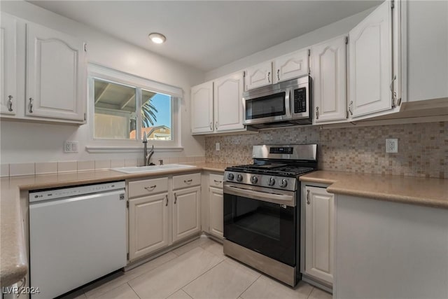 kitchen featuring sink, tasteful backsplash, light tile patterned flooring, white cabinets, and appliances with stainless steel finishes