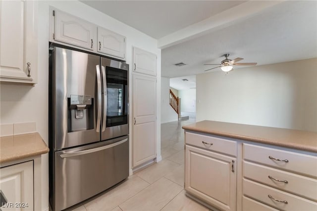 kitchen featuring ceiling fan, stainless steel fridge, light tile patterned flooring, and white cabinetry