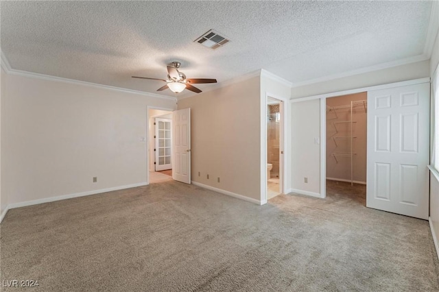 unfurnished bedroom featuring crown molding, ensuite bath, ceiling fan, a spacious closet, and a closet