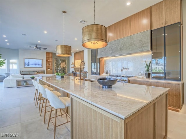 kitchen with a large island, sink, light stone countertops, decorative light fixtures, and stainless steel gas stovetop