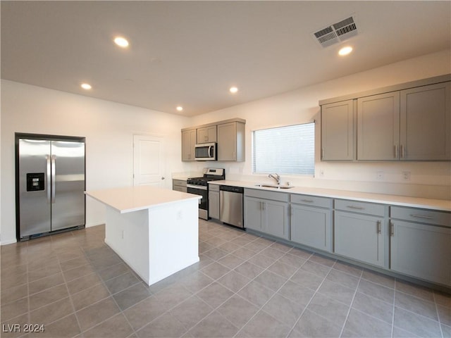 kitchen featuring stainless steel appliances, sink, light tile patterned floors, gray cabinets, and a kitchen island