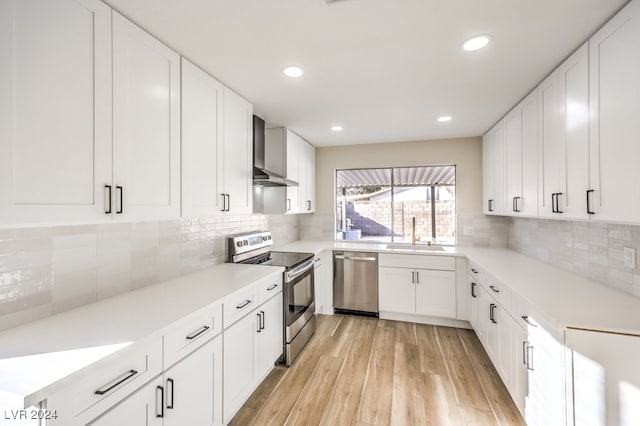 kitchen with appliances with stainless steel finishes, backsplash, sink, wall chimney range hood, and white cabinets