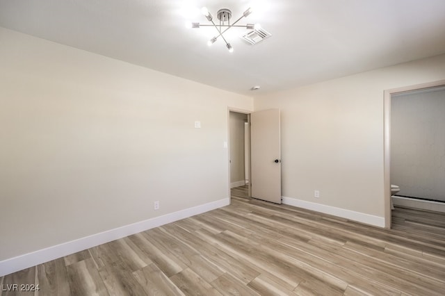 unfurnished bedroom featuring ensuite bathroom, a baseboard radiator, and light wood-type flooring