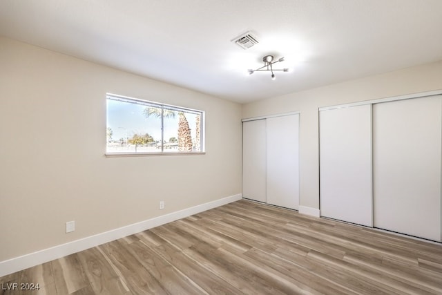 unfurnished bedroom with light hardwood / wood-style flooring and multiple closets