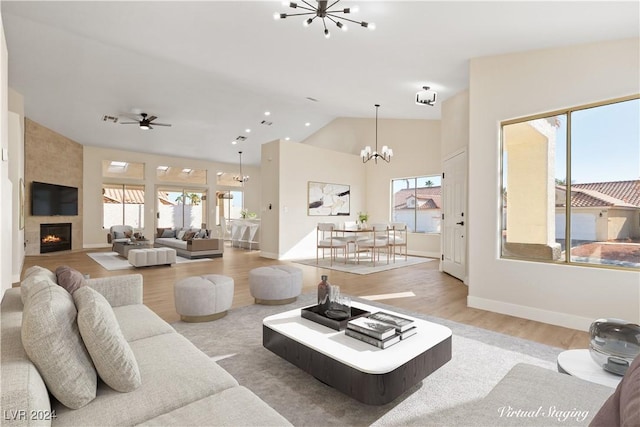 living room with ceiling fan with notable chandelier, vaulted ceiling, a large fireplace, and light hardwood / wood-style flooring