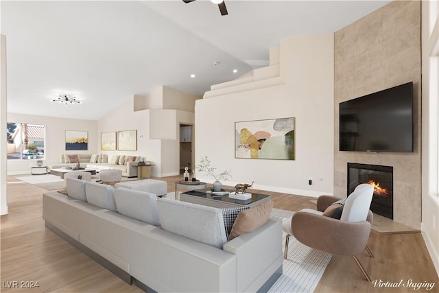 living room with a fireplace, light wood-type flooring, ceiling fan, and lofted ceiling