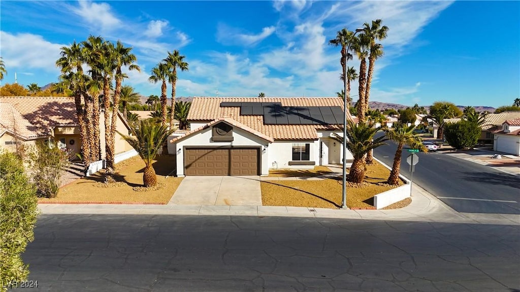 view of front of home featuring an attached garage, solar panels, a tiled roof, driveway, and stucco siding