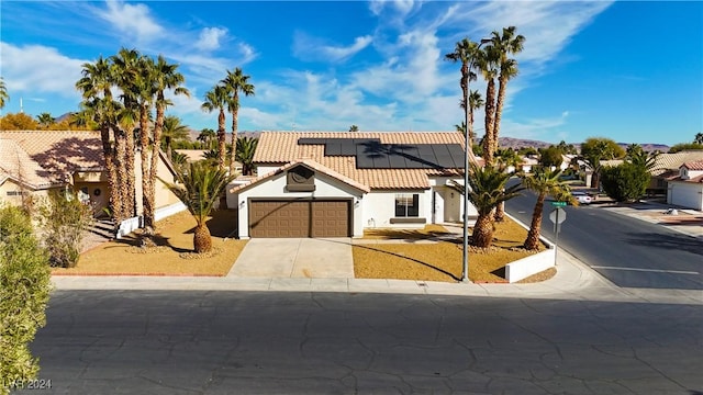 view of front of home featuring an attached garage, solar panels, a tiled roof, driveway, and stucco siding