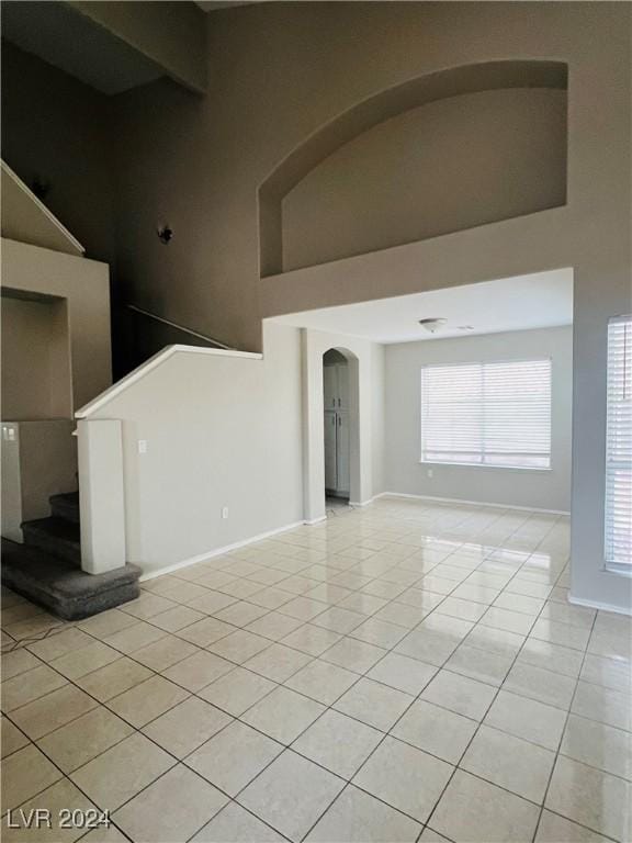 unfurnished living room with light tile patterned flooring, plenty of natural light, and a high ceiling