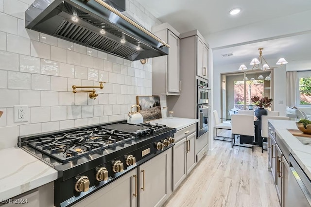 kitchen with appliances with stainless steel finishes, gray cabinetry, backsplash, light stone counters, and ventilation hood