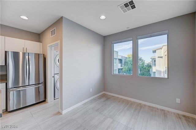 kitchen featuring stacked washer / dryer, stainless steel refrigerator, and white cabinets