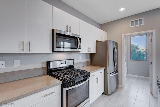 kitchen featuring appliances with stainless steel finishes, white cabinetry, light tile patterned floors, and light stone countertops