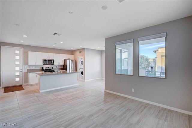 kitchen featuring stainless steel appliances, sink, a center island with sink, stacked washer and clothes dryer, and white cabinets