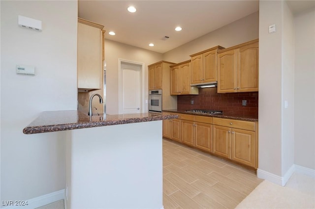 kitchen with backsplash, dark stone counters, sink, kitchen peninsula, and stainless steel appliances