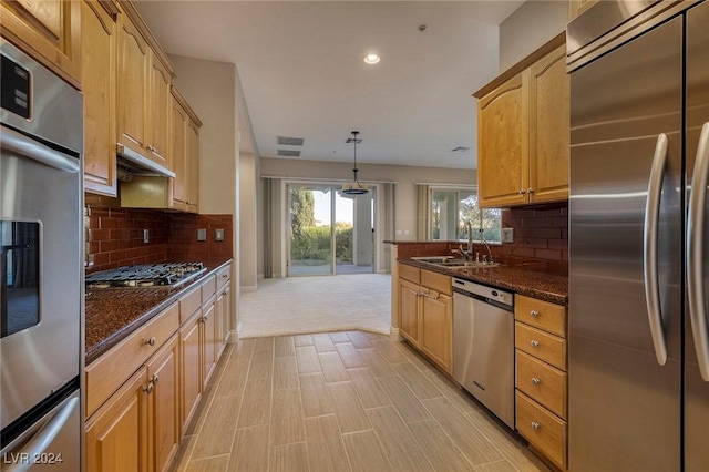 kitchen featuring backsplash, dark stone counters, stainless steel appliances, sink, and hanging light fixtures