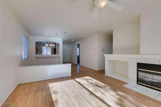 unfurnished living room featuring a fireplace, ceiling fan with notable chandelier, light hardwood / wood-style flooring, and built in features