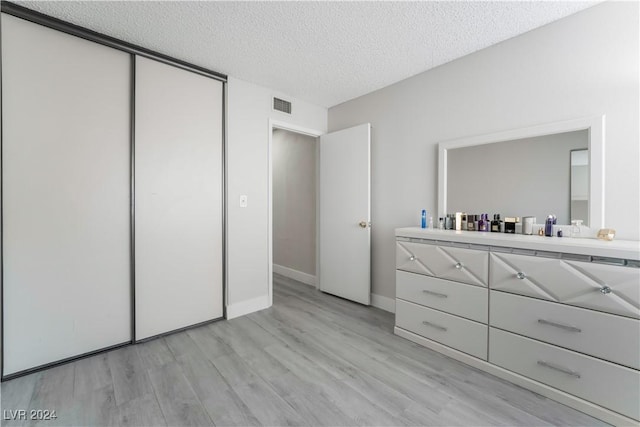 unfurnished bedroom with light wood-type flooring, a textured ceiling, and a closet