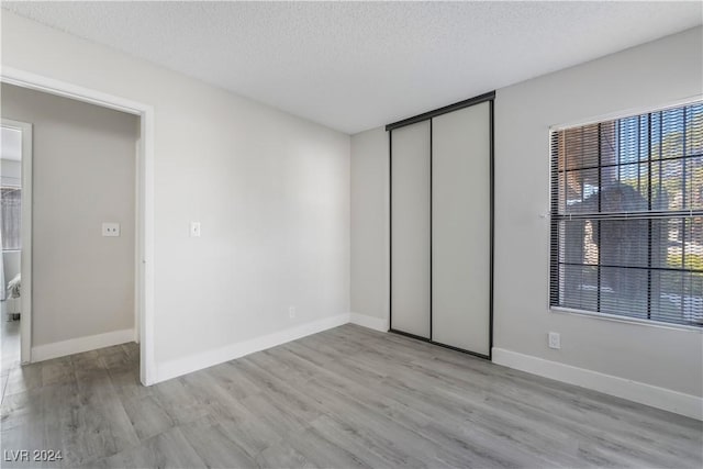 unfurnished bedroom featuring a textured ceiling, light hardwood / wood-style flooring, and a closet