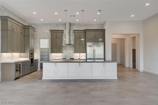 kitchen featuring a kitchen island with sink, wall chimney range hood, decorative light fixtures, stainless steel appliances, and beverage cooler