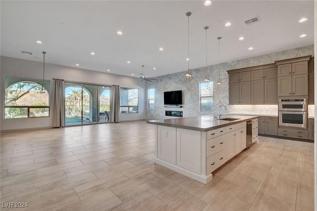 kitchen featuring ceiling fan, sink, pendant lighting, a kitchen island with sink, and white cabinets