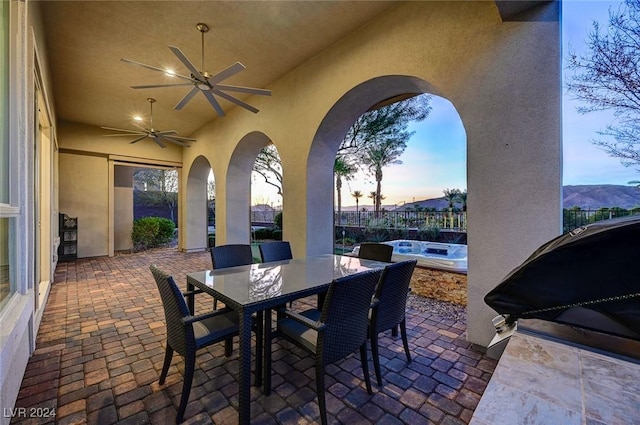 patio terrace at dusk with a mountain view, ceiling fan, and grilling area