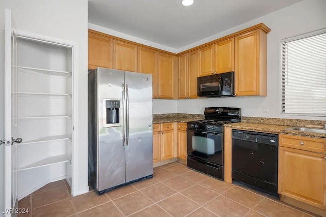 kitchen featuring a sink, black appliances, light tile patterned floors, and dark stone counters