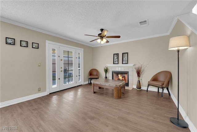 sitting room featuring ceiling fan, wood-type flooring, ornamental molding, and a tile fireplace