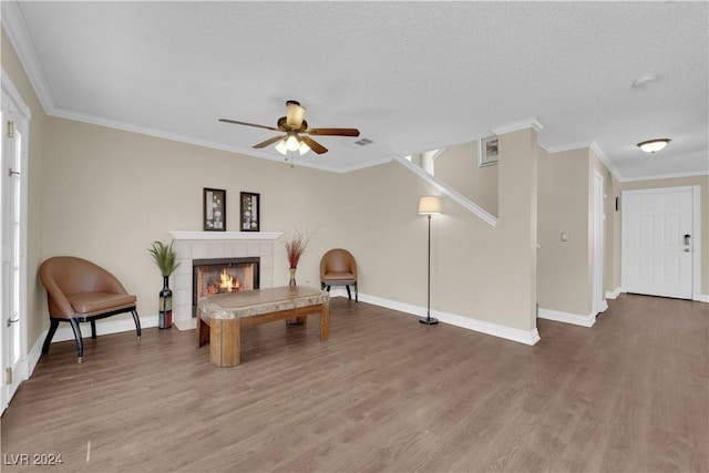 living area with a tile fireplace, ceiling fan, ornamental molding, a textured ceiling, and hardwood / wood-style flooring