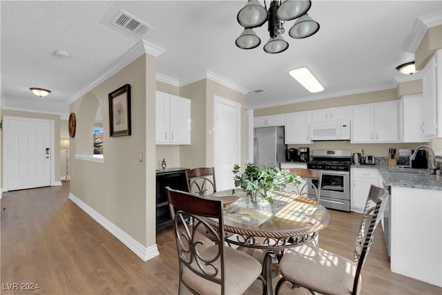 dining room with sink, an inviting chandelier, light wood-type flooring, a textured ceiling, and ornamental molding