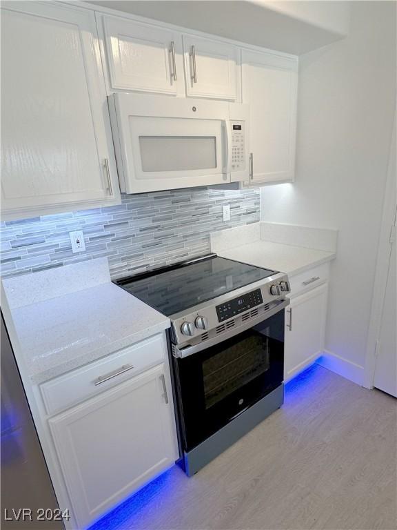 kitchen with tasteful backsplash, white microwave, stainless steel range with electric cooktop, light wood-type flooring, and white cabinetry