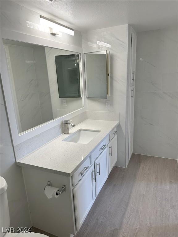 bathroom with toilet, a textured ceiling, wood finished floors, and vanity