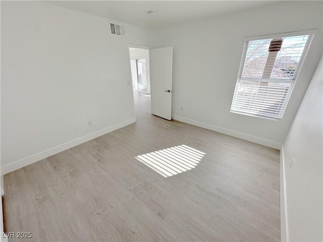 spare room featuring light wood-style flooring, visible vents, and baseboards