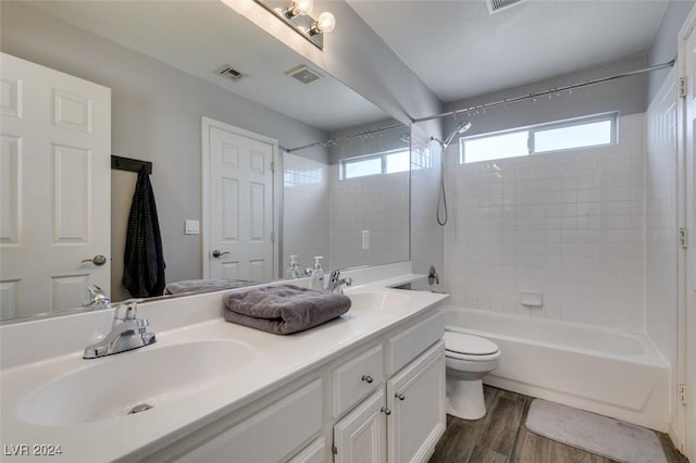 full bathroom featuring vanity, hardwood / wood-style floors, tiled shower / bath combo, and toilet