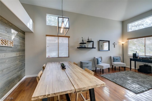 dining space featuring wooden walls, hardwood / wood-style floors, and a high ceiling