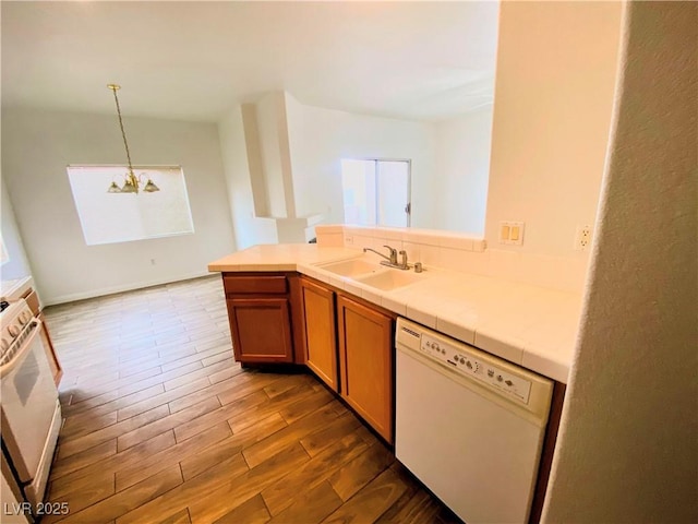 kitchen featuring wood-type flooring, sink, a chandelier, hanging light fixtures, and white dishwasher